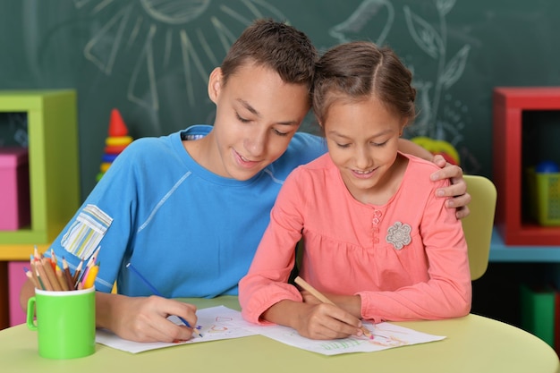 Hermano y hermana sonrientes dibujando con lápices de colores juntos en el interior