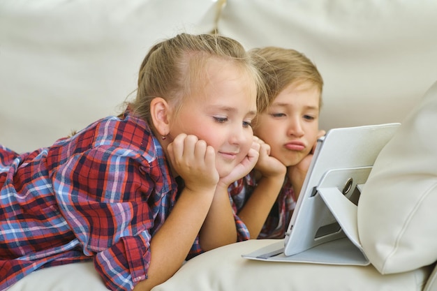 Hermano y hermana sonrientes con tableta en el sofá de la sala de estar