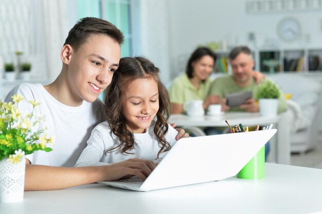 Hermano y hermana usando una computadora portátil mientras están sentados en la mesa