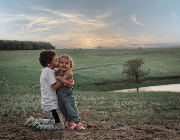 El hermano mayor besa a su hermana pequeña en el contexto de un paisaje pintoresco.