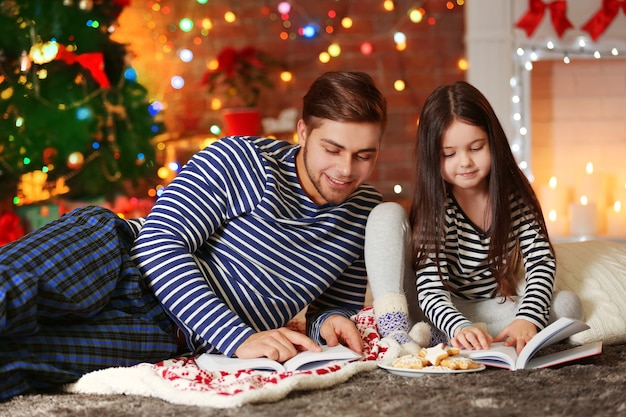 Hermano mayor con hermanita leyendo libros y comiendo galletas en el salón de Navidad