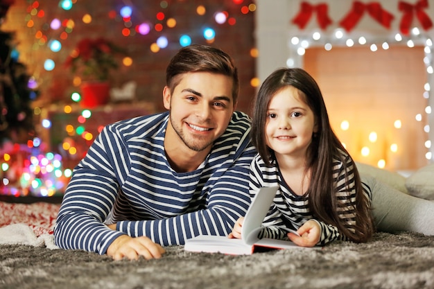 Hermano mayor con el libro de lectura de la hermana pequeña en el salón de Navidad