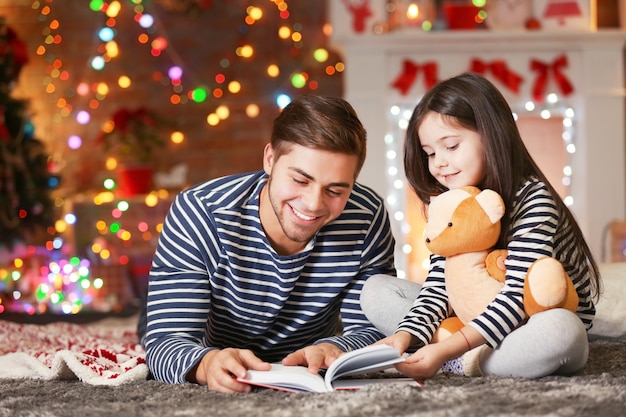 Hermano mayor con el libro de lectura de la hermana pequeña en el salón de Navidad