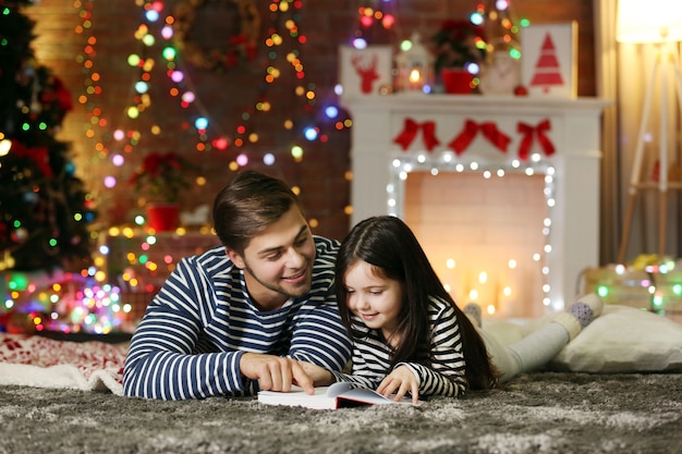 Hermano mayor con el libro de lectura de la hermana pequeña en el salón de Navidad