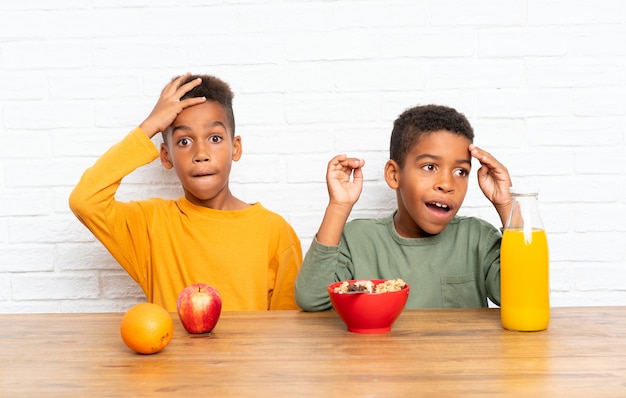 Hermanos afroamericanos desayunando y haciendo gesto de sorpresa