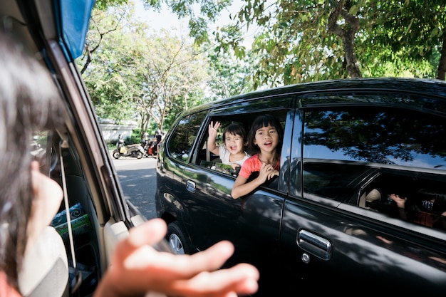 Hermanos asiáticos agitando las manos desde la ventana y viajan en coche