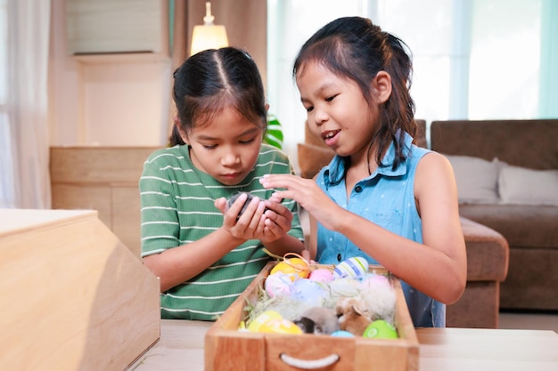 Los hermanos asiáticos juegan con un conejito y decoran los huevos de Pascua preparándose para la Pascua en casa juntos con diversión Familia feliz Felices Pascuas Felices vacaciones