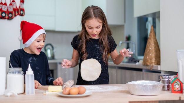 Los hermanos están cocinando en la cocina, el niño con sombrero de Navidad, la niña está vomitando la masa. Idea de niños felices