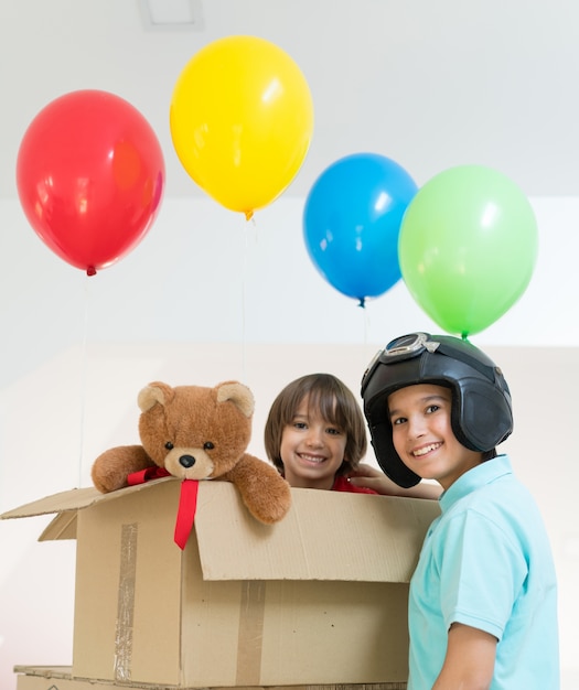 Hermanos felices jugando con globos y caja de cartón