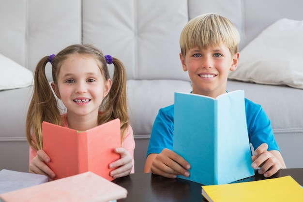 Hermanos felices leyendo libros en el piso