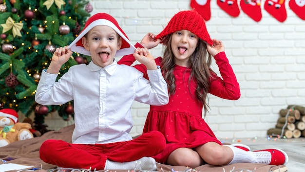 Hermanos felices en trajes de Navidad en el suelo cerca del árbol de Navidad en casa. Idea de familia feliz