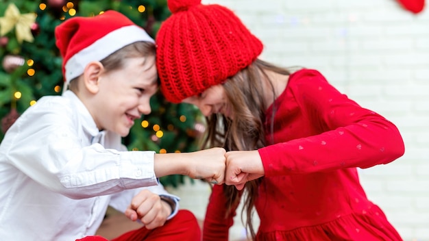 Hermanos felices en trajes de Navidad en el suelo cerca del árbol de Navidad en casa. Idea de familia feliz