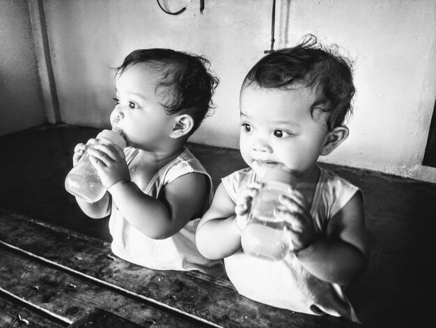 Hermanos lindos bebiendo leche de botellas en casa