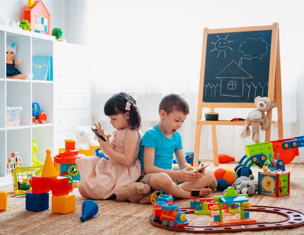 Hermanos en el piso jugando con teléfonos inteligentes