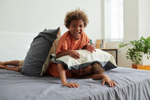 Hermanos preadolescentes luchando con almohadas en la cama de los padres