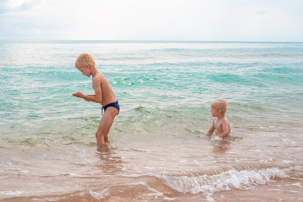 Hermanos rubios jugando en el agua de mar en una playa de arena en un día de verano Vacaciones divertidas