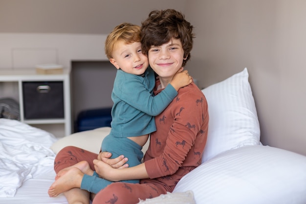 Hermanos sentados en una cama por la mañana después de despertarse y abrazarse. Hermano mayor tierno. Familia feliz.