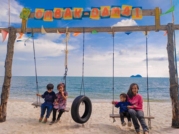 Foto hermanos sentados en columpios en la playa