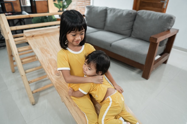 Los hermanos siguen jugando pacientemente el tobogán del juguete triángulo pikler juntos en la sala de estar