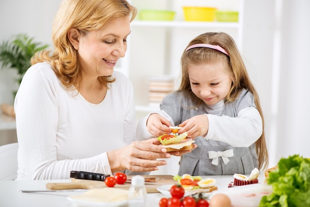 Hermosa abuela feliz y su linda nieta haciendo un sándwich en la cocina.