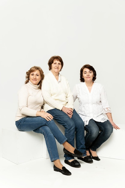 Hermosa abuela sonríe estando en un fondo blanco con sus hijas. grupo de mujeres felices. la abuela abraza a su hija. dia familiar