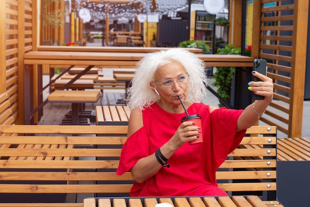 Hermosa abuela se toma una selfie en su teléfono y bebe café