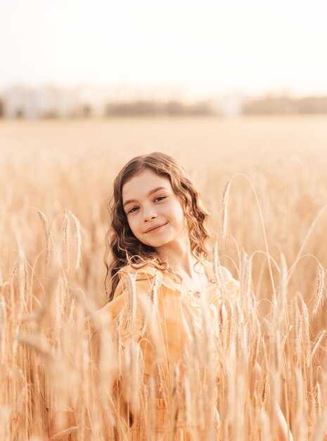 Hermosa adolescente con cabello largo caminando por un campo de trigo en un día soleado. Retrato al aire libre. Colegiala relajante