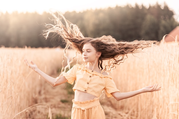 Hermosa adolescente con cabello largo caminando por un campo de trigo en un día soleado. Retrato al aire libre. Colegiala relajante