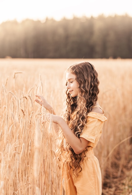 Hermosa adolescente con cabello largo caminando por un campo de trigo en un día soleado. Retrato al aire libre. Colegiala relajante