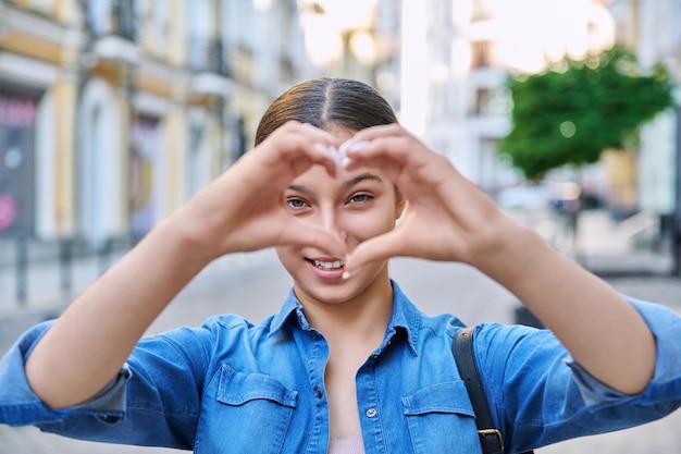 Hermosa adolescente feliz mostrando el signo del corazón con las manos al aire libre en la ciudad