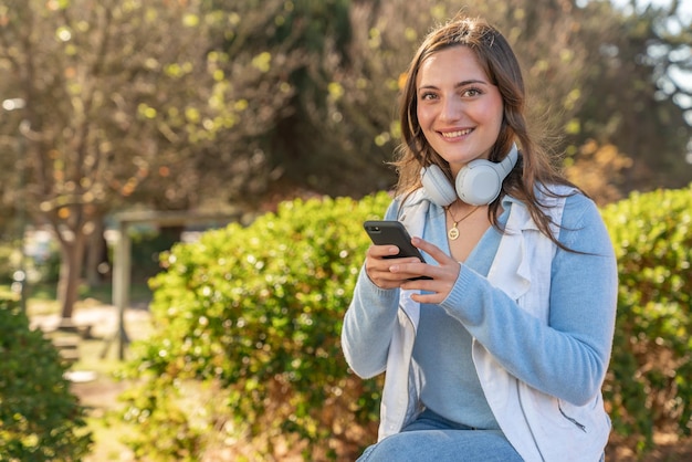 Foto hermosa adolescente feliz usando su teléfono móvil en un parque durante la tarde