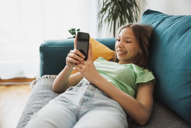 Hermosa adolescente navegando por las redes sociales en un teléfono inteligente mientras tiene tiempo libre en su casa.