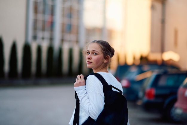 Una hermosa adolescente rubia regresa a casa de la escuela durante la puesta de sol llevando su mochila escolar