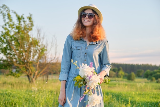 Hermosa adolescente en sombrero de vestir de mezclilla con ramo de flores silvestres