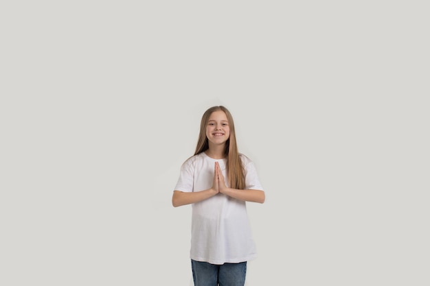 Una hermosa adolescente sostiene sus palmas contra su pecho sobre un fondo blanco aislado.