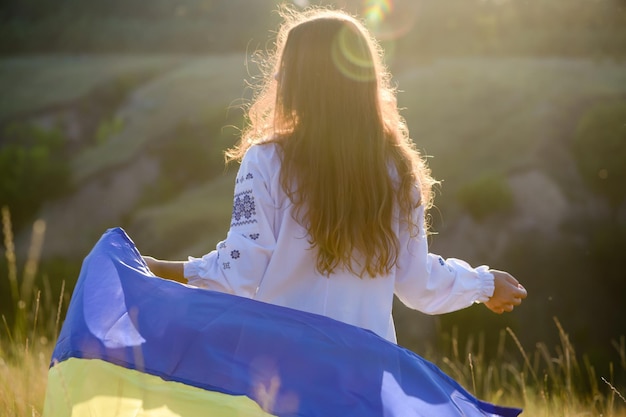 Una hermosa adolescente vestida con ropa nacional ondeando la bandera ucraniana