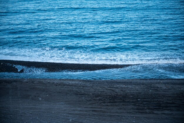 Hermosa agua tranquila y pacífica que fluye con olas hacia la playa con árboles verdes contra el cielo azul nublado durante el día sin gente alrededor