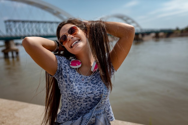Una hermosa y alegre chica divirtiéndose con su cabello al aire libre y disfrutando en la orilla del río de la ciudad en un hermoso día de verano.