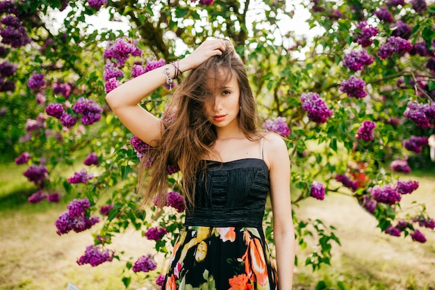 Hermosa y alegre expresiva joven morena posando delante del árbol lila floreciente. Tiempo de primavera