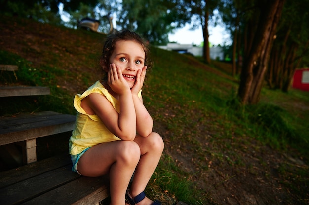 Hermosa y alegre niña sentada en un escalón de madera junto al muelle del lago