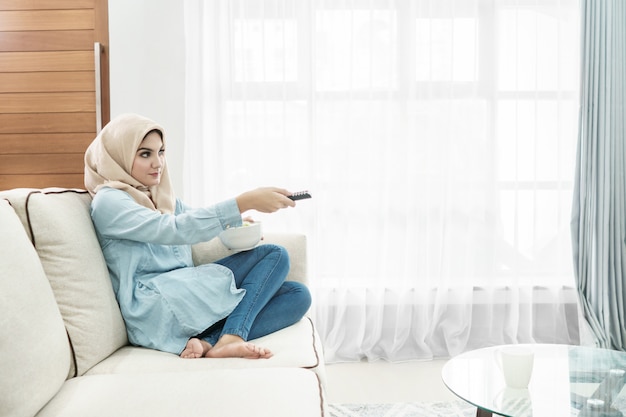 Hermosa ama de casa vistiendo hijab viendo televisión en un leisu