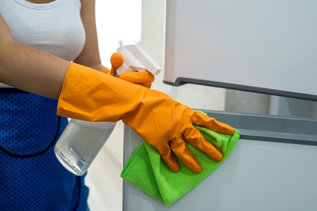 Hermosa ama de llaves limpiando las puertas del refrigerador con un trapo