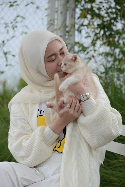 Hermosa amante de los gatos musulmanes asiáticos jugando con su gato al aire libre