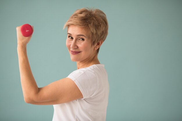 Hermosa anciana en camiseta blanca entra para deportes con mancuernas