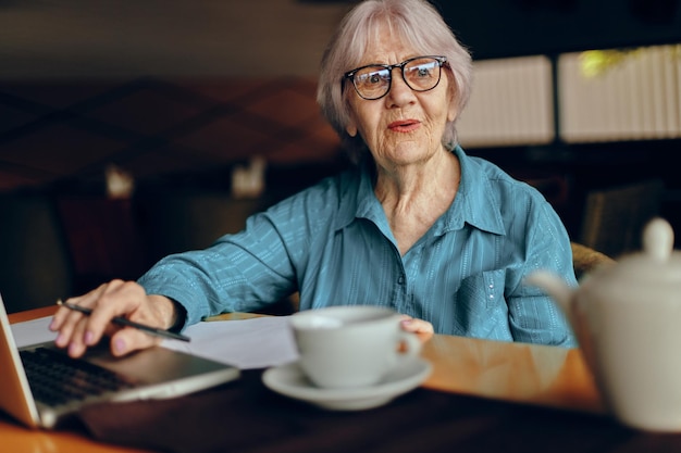 Hermosa anciana madura con gafas se sienta en una mesa frente a una computadora portátil sin alteraciones