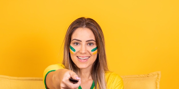 Hermosa animadora brasileña rubia con el control remoto viendo el partido de Brasil