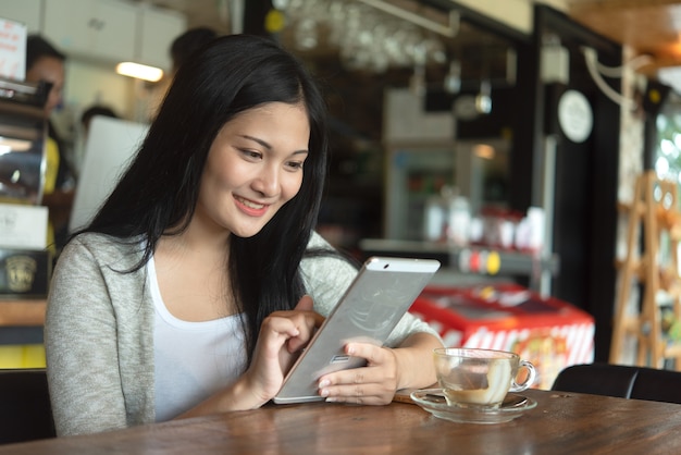 Hermosa atractiva joven mujer asiática con teléfono inteligente en la cafetería