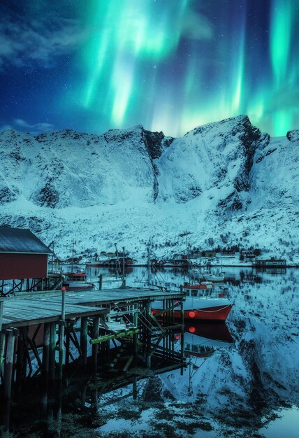 Hermosa aurora borealis auroras boreales sobre montañas cubiertas de nieve y pueblo de pescadores en el círculo polar ártico en las islas Lofoten Noruega