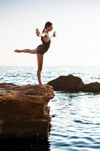 Hermosa bailarina bailando posando sobre roca en el fondo del mar de playa