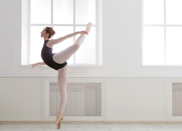 Hermosa bailarina se encuentra en posición de ballet arabesco